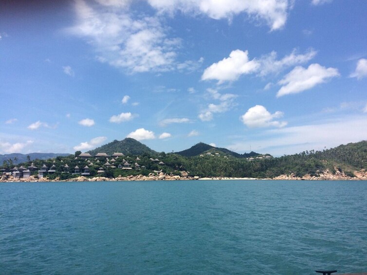 A coastal landscape with a clear sky, a body of water, and a hill with buildings. 2