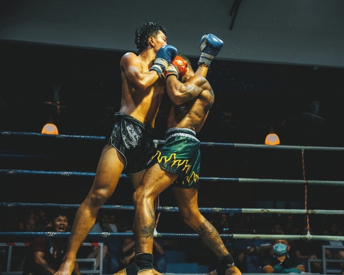 Dos boxeadores en un ring, uno con shorts negros con un diseño de dragón y el otro con shorts verdes con patrones amarillos. 1