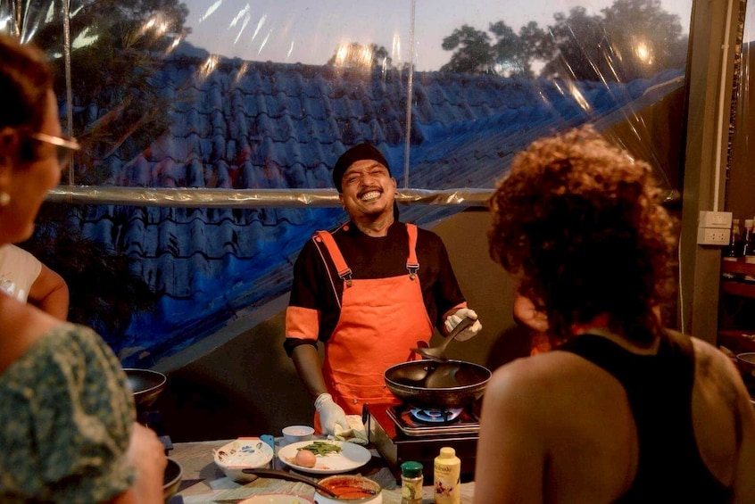 Un vendeur de nourriture de rue préparant des plats à un stand, entouré de clients. 3