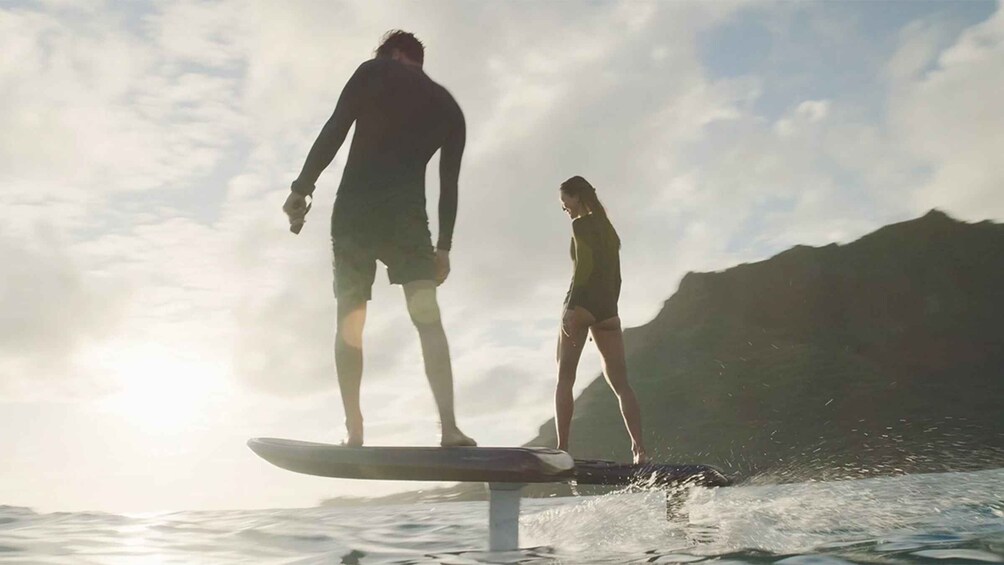 Two people surfing on a wave with mountains in the background. 2