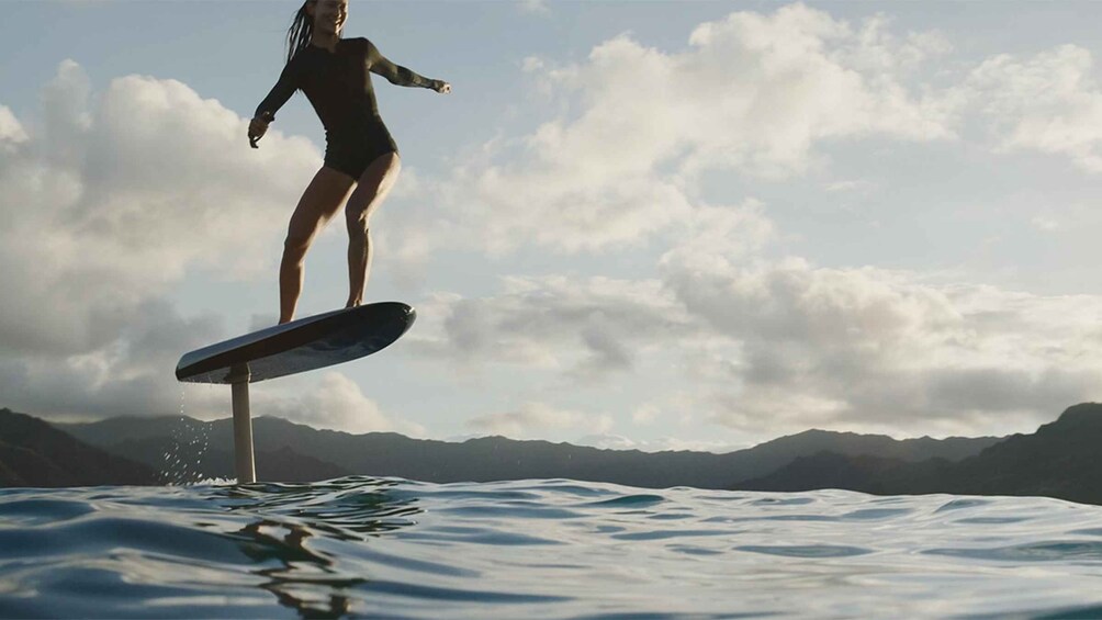 A person surfing on a wave with mountains in the background. 1