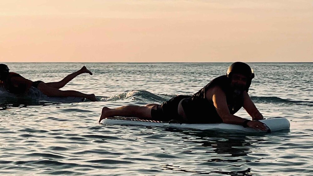 Two people lying on surfboards in the ocean during sunset. 5