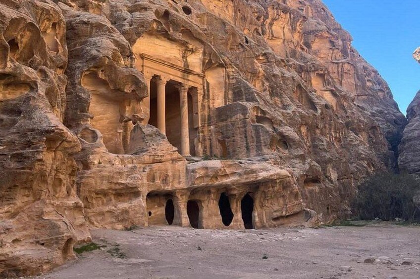 A rock-cut structure with columns and a facade, surrounded by rugged terrain. 5