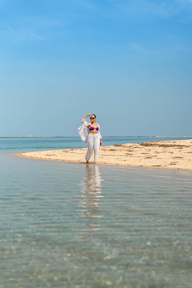 A person standing on a beach with clear water and a distant shoreline. 2
