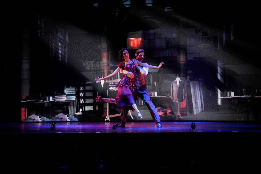A couple performing a dance on a stage with a dark, industrial backdrop. 2