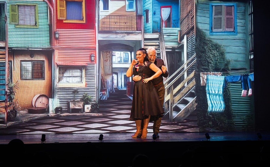 A stage with a couple embracing, set against a backdrop of colorful, multi-story buildings. 3