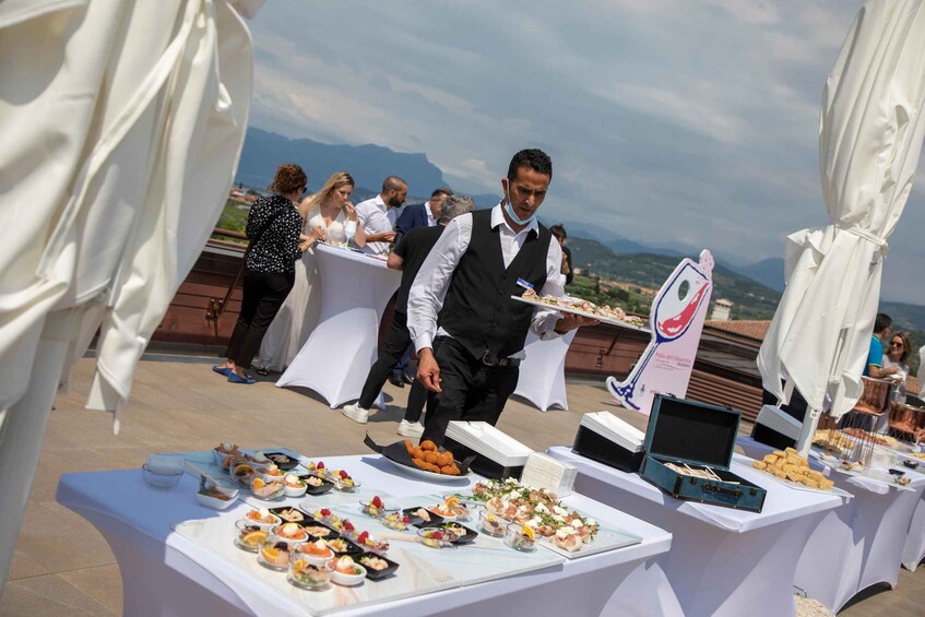 A catering setup with various dishes on tables, a waiter carrying a tray, and a scenic mountain backdrop. 2
