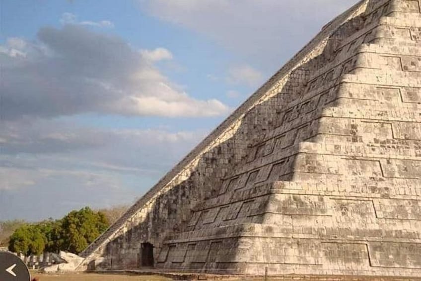 A large stone pyramid with hieroglyphs, surrounded by trees and a clear sky. 1