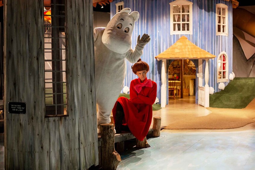 A person in a red coat sitting on a wooden bench next to a life-sized bear statue. 1