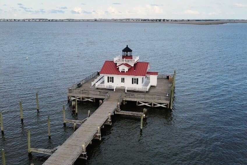 A lighthouse on a wooden pier extending into calm water. 4