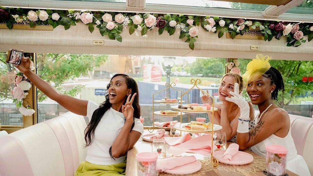 A group of people at a table with a tiered dessert stand, surrounded by a floral canopy. 1