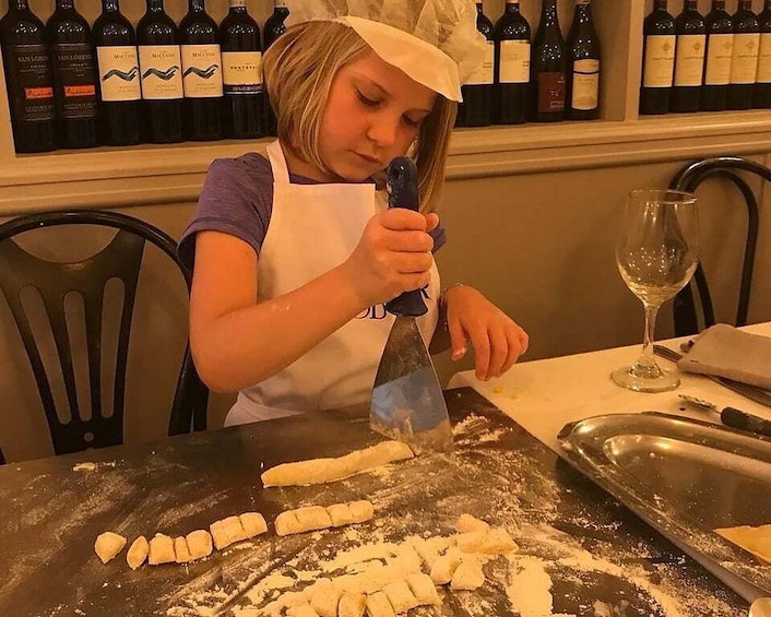 A person slicing dough on a table with a pizza cutter, surrounded by wine bottles. 5