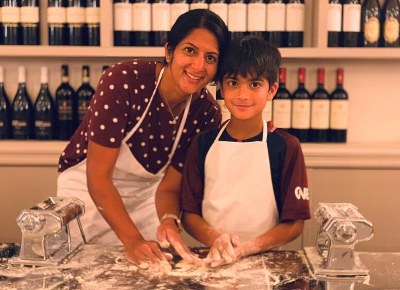 Two people kneading dough with flour on a marble countertop, surrounded by wine bottles in the background. 3