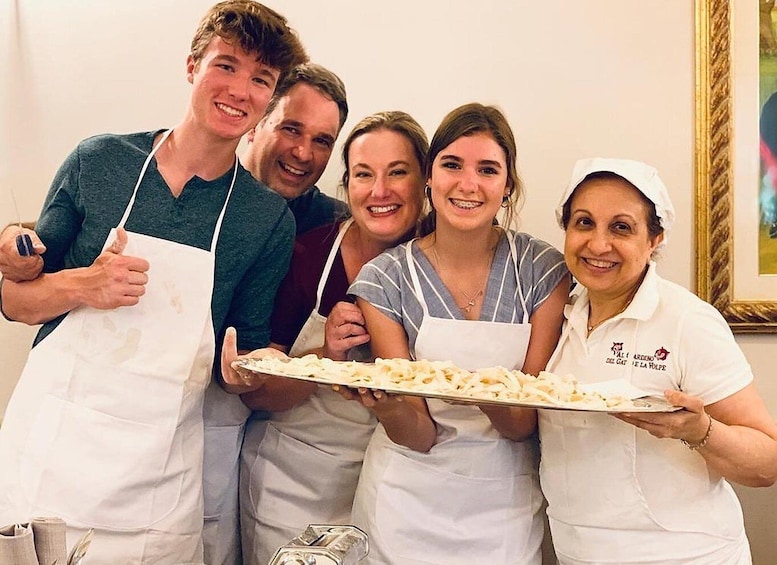 A group of people wearing aprons, holding a large tray of food, and posing for a photo. 4