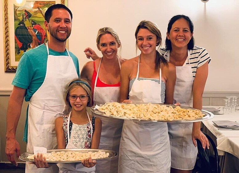 A family of five in a kitchen, each wearing an apron, holding trays of food. 1