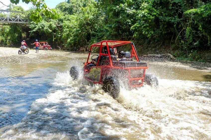 Un véhicule tout-terrain rouge traverse une rivière peu profonde, projetant de l’eau tout autour. 3