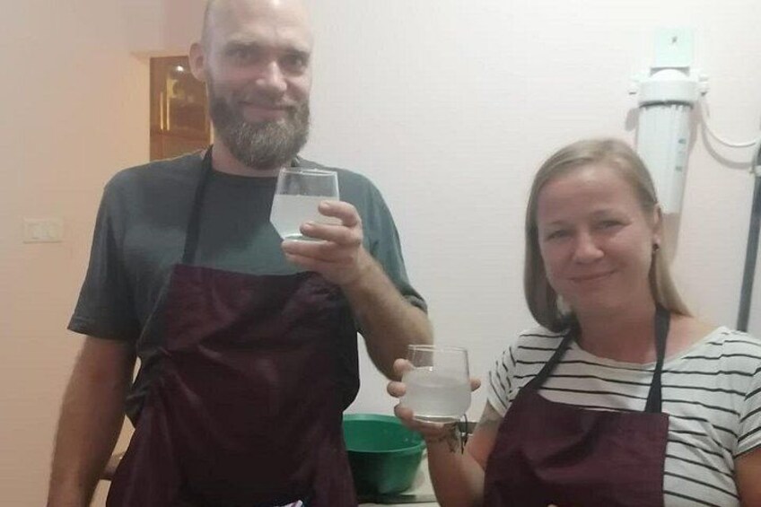 Two people wearing aprons, holding glasses of water, in a room with a white wall and a green bowl on a table. 3