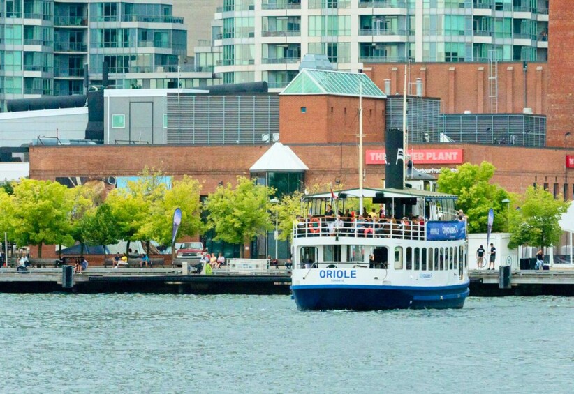 Een boot genaamd ORIOLE op een rivier, met een stadsgezicht op de achtergrond, inclusief een gebouw met een bord waarop  4