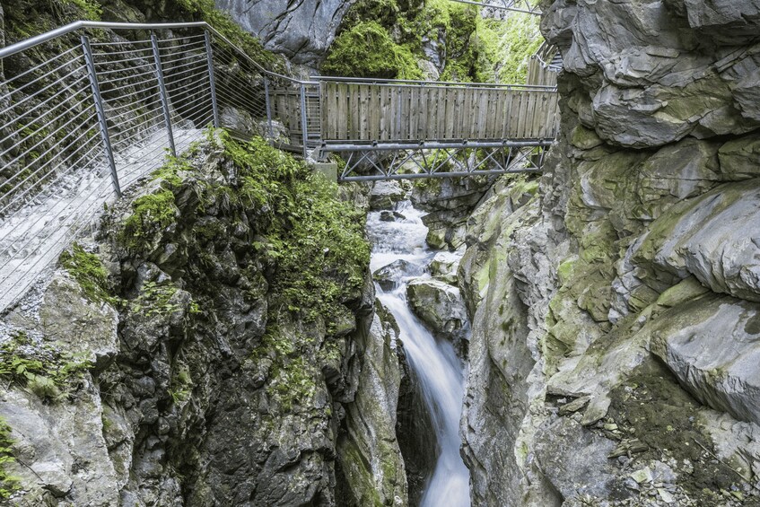 A wooden bridge over a rocky gorge with a flowing stream. 2