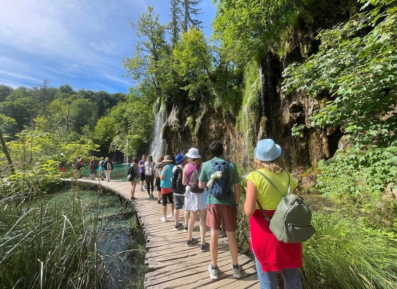 Un grupo de personas caminando sobre un puente de madera que cruza un río, rodeado de exuberante vegetación y acantilados rocosos. 4
