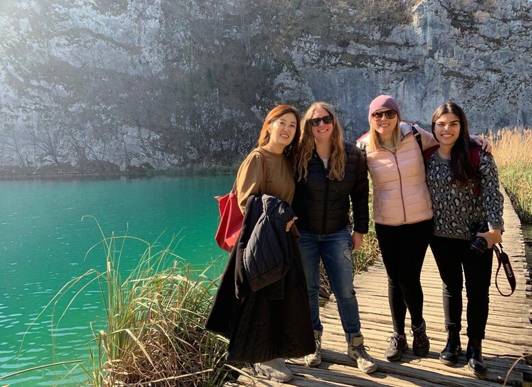 Cuatro personas sobre un muelle de madera junto a un lago turquesa con acantilados rocosos al fondo. 2