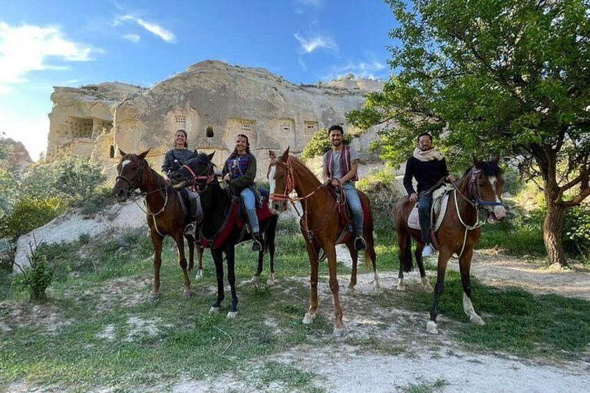 Cuatro personas montando a caballo por un sendero de tierra, con un edificio histórico al fondo. 2