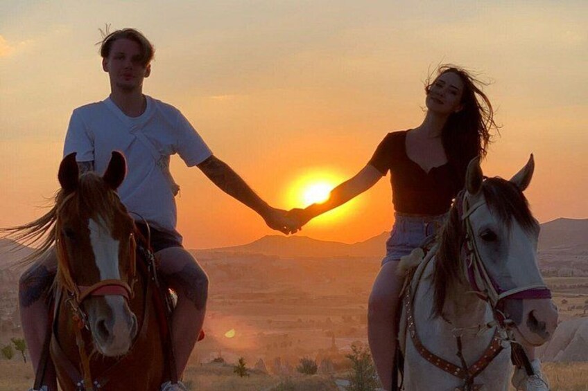 Dos personas tomadas de la mano montando a caballo al atardecer. 3