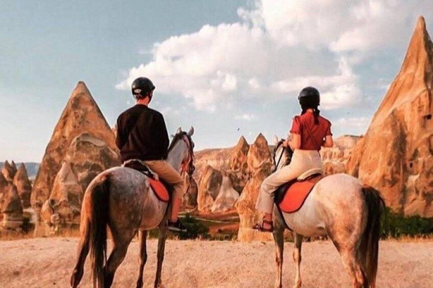 Dos personas montando a caballo sobre terreno rocoso con formaciones geológicas únicas al fondo. 1