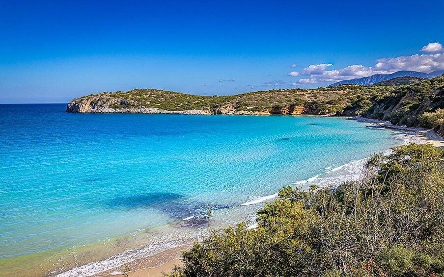 A coastal landscape with clear turquoise waters, sandy beach, and green hills. 3