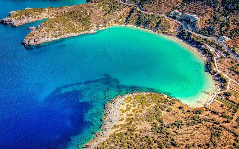 An aerial view of a coastal area with turquoise waters, rocky islands, and a road leading to a building. 1
