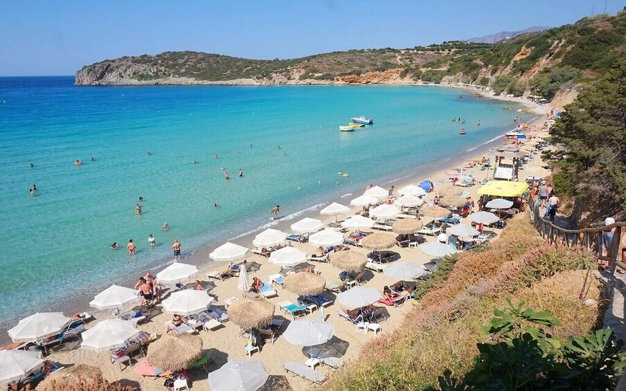A beach with clear turquoise water, umbrellas, and people sunbathing. 5