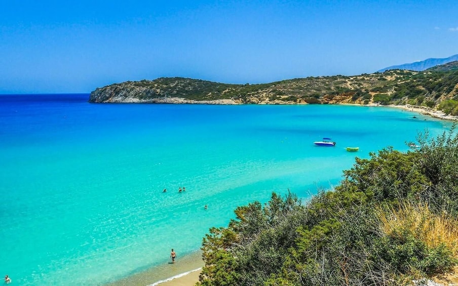 A turquoise sea with boats, a beach, and hills in the background. 4