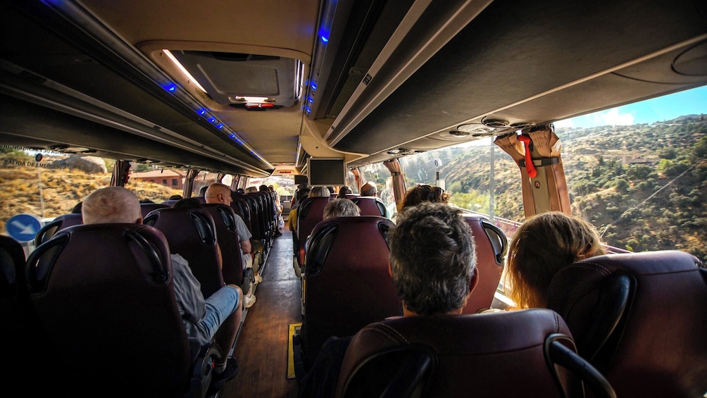 The interior of a bus with passengers seated and looking out at a mountainous landscape. 5