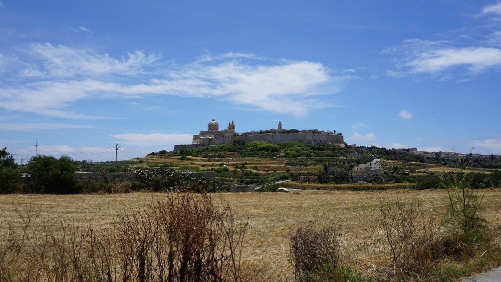 A hilltop fortress with a prominent dome and towers, surrounded by dry grassland and distant buildings. 4