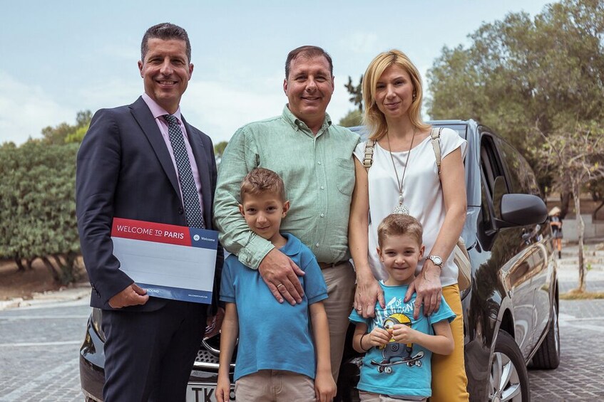 A family posing with a welcome sign and a car. 3