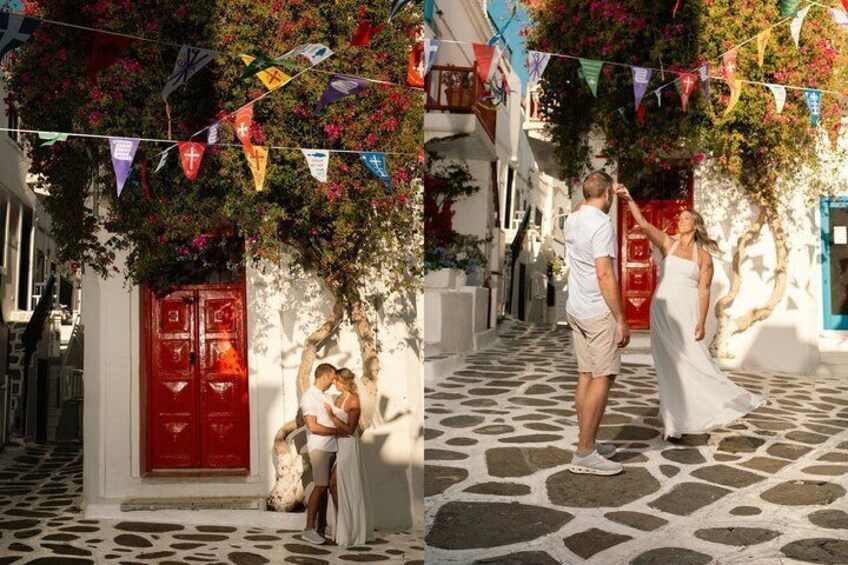 Una pareja caminando por una calle adoquinada en un pueblo mediterráneo, con banderas coloridas y una puerta roja. 5