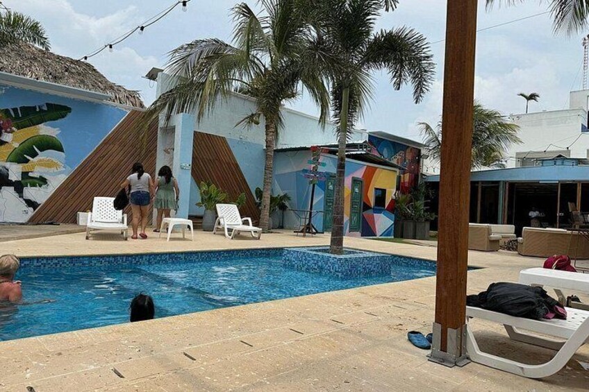 A swimming pool with lounge chairs, palm trees, and a mural on the wall. 2