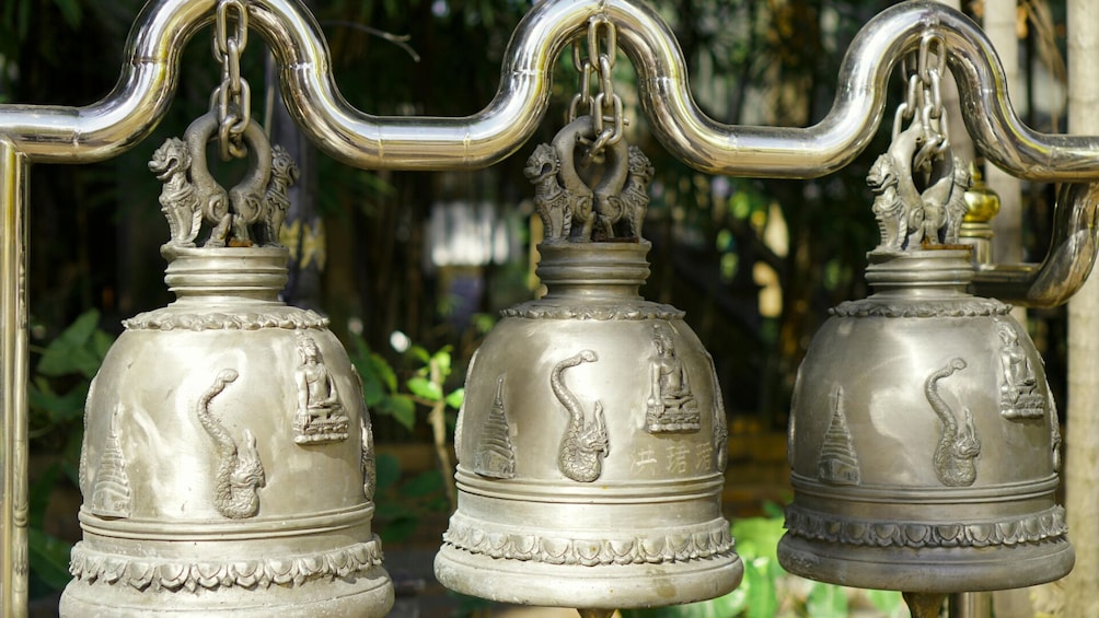 Three metal bells with swan designs, mounted on a metal structure. 3