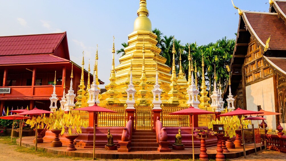 A golden stupa surrounded by white and gold spires, with red umbrellas and potted plants in front. 4