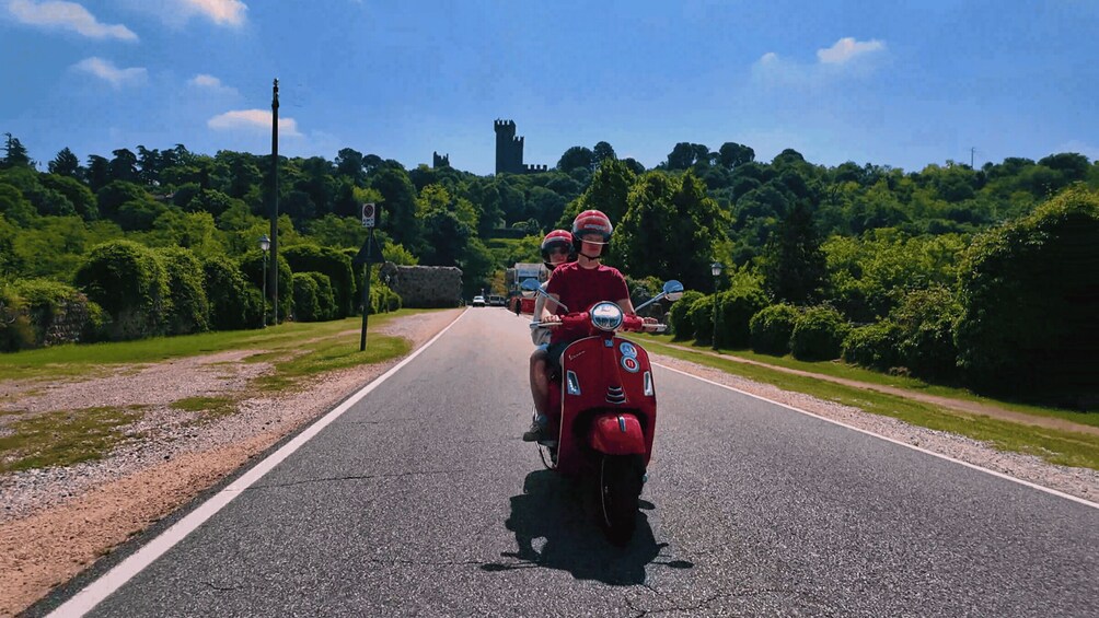 Two people on a red scooter on a road with a castle in the background. 4
