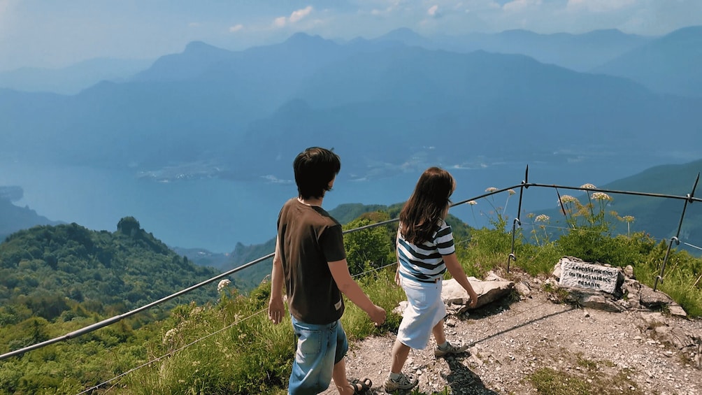 Two people standing on a rocky outcrop overlooking a mountainous landscape with a body of water in the distance. 5