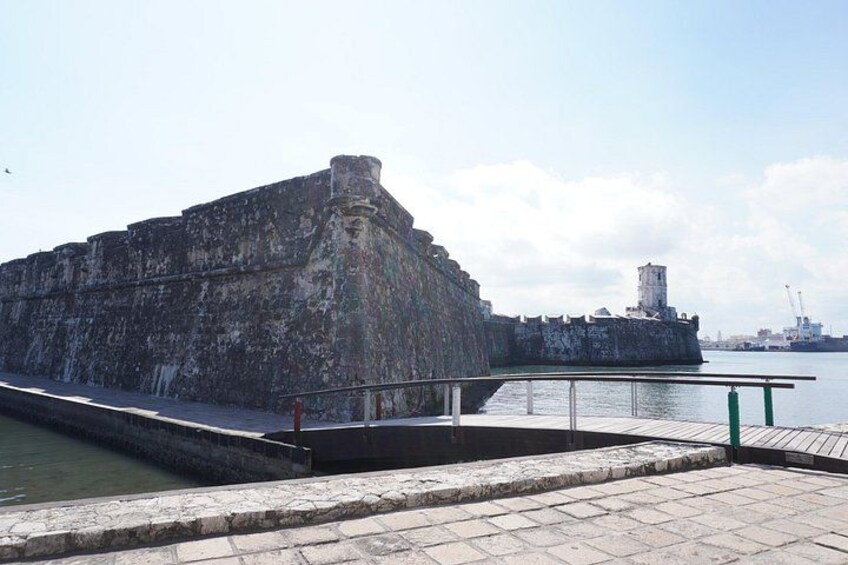 Un'imponente fortificazione in pietra sul lungomare, una piccola torre e un vialetto lastricato. 4