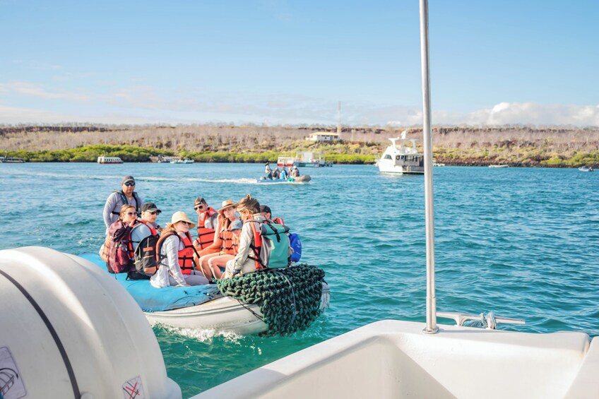 Un grupo de personas en un bote, con chalecos salvavidas, un mar tranquilo y una costa lejana con vegetación escasa. 4