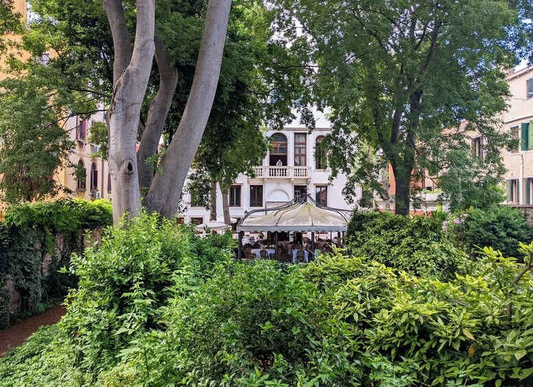 A lush garden with dense foliage, a gazebo, and a white building with balconies. 2