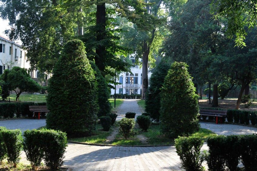A park with a paved path, neatly trimmed hedges, and a building in the background. 5