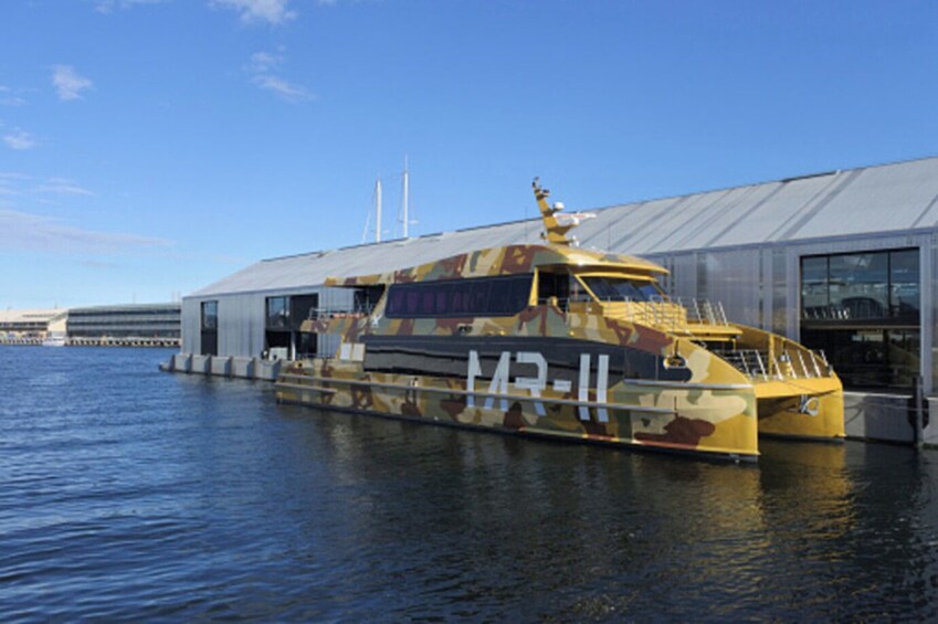 Un barco grande y camuflado amarrado a un muelle, con un edificio al fondo. 3