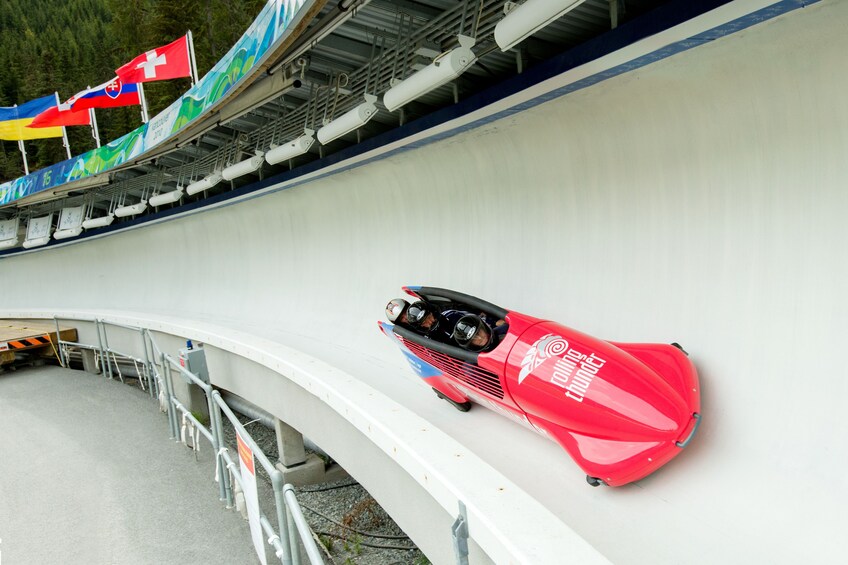 Un trineo bobsleigh rojo en una pista con banderas y un diseño azul y blanco. 1