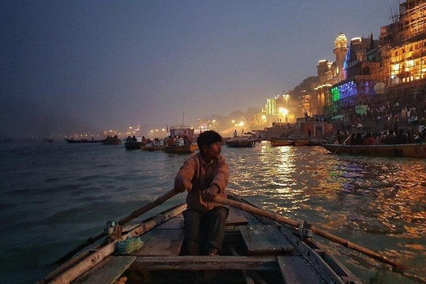 A person rowing a boat on a river with buildings and lights in the background. 2