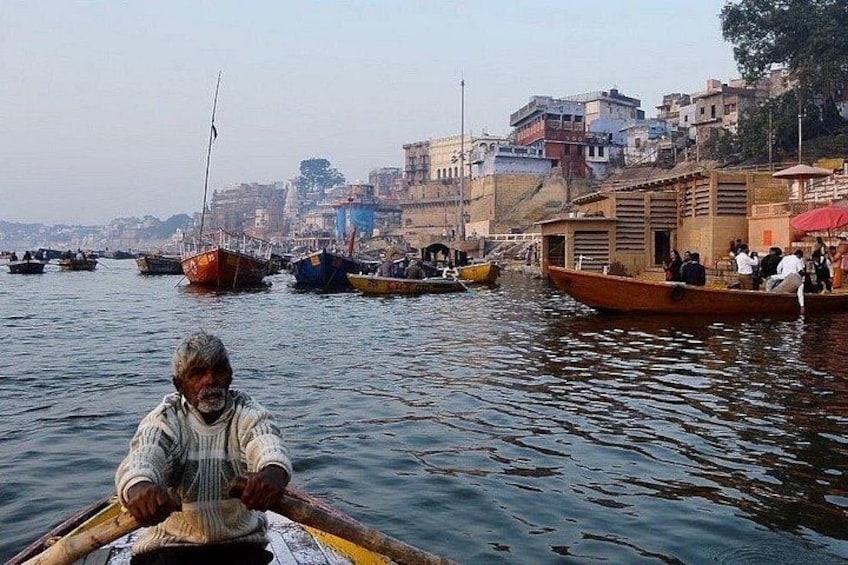 A river with boats, a person rowing a boat, and buildings along the riverbank. 1