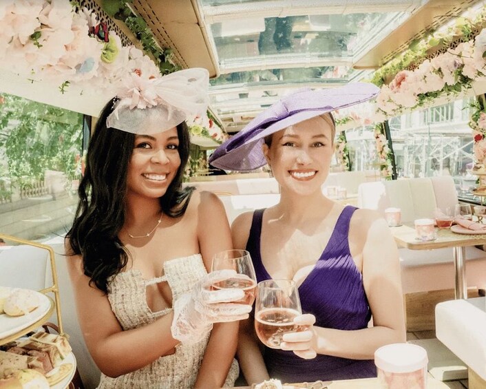Two women at a table with drinks, surrounded by floral decorations and a glass ceiling. 4